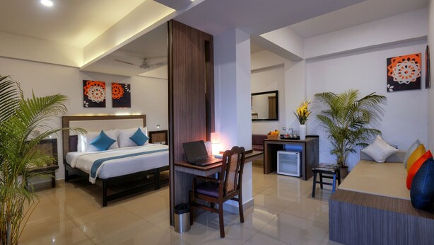 A hotel room with a bed, desk, chair, and a small refrigerator.