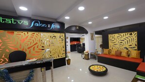 A reception area with a sign reading "Tatva Salon & Spa," a reception desk, a seating area with a sofa and cushions, and a decorative flower arrangement on the floor.