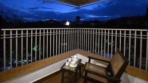 A balcony with a table set for tea, a chair, and a view of a distant lit building at dusk.