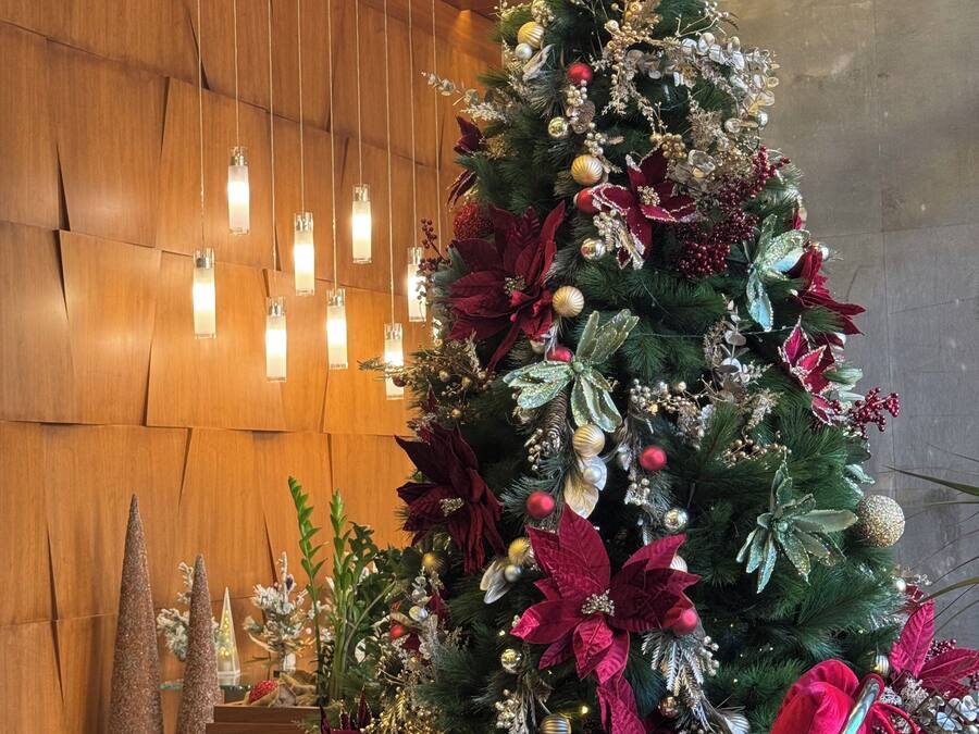 Un árbol de Navidad adornado con adornos y flores de Pascua, una pared de madera y luces colgantes.