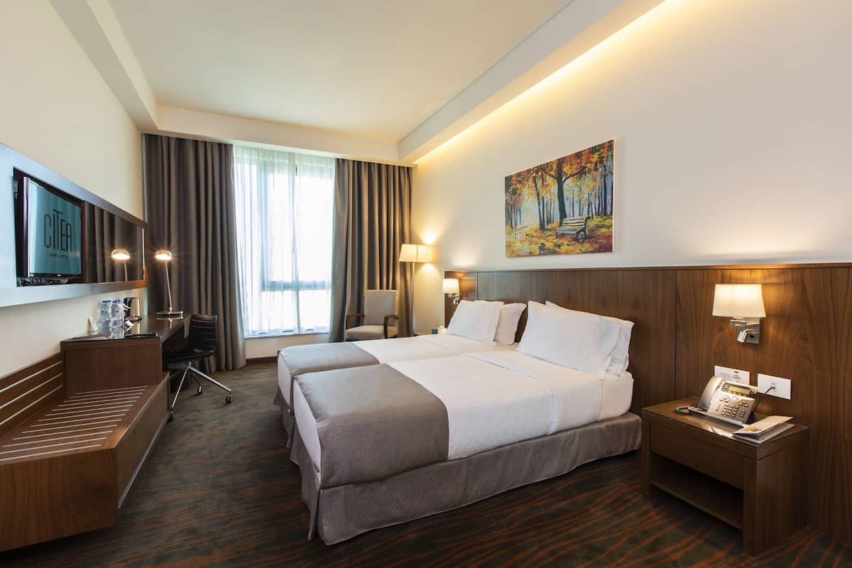 A hotel room with a large bed, a desk, a chair, a TV, and a painting on the wall.