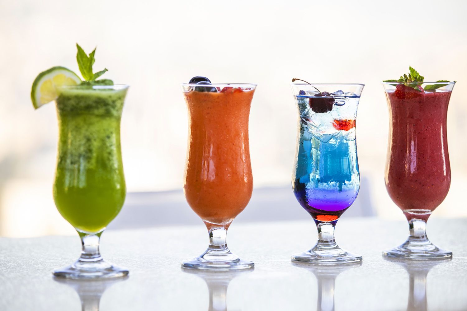 Four colorful cocktails in tall glasses.