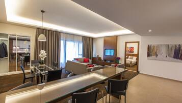 A modern hotel room with a dining area, a living room with a sofa and TV, and a large mirror.