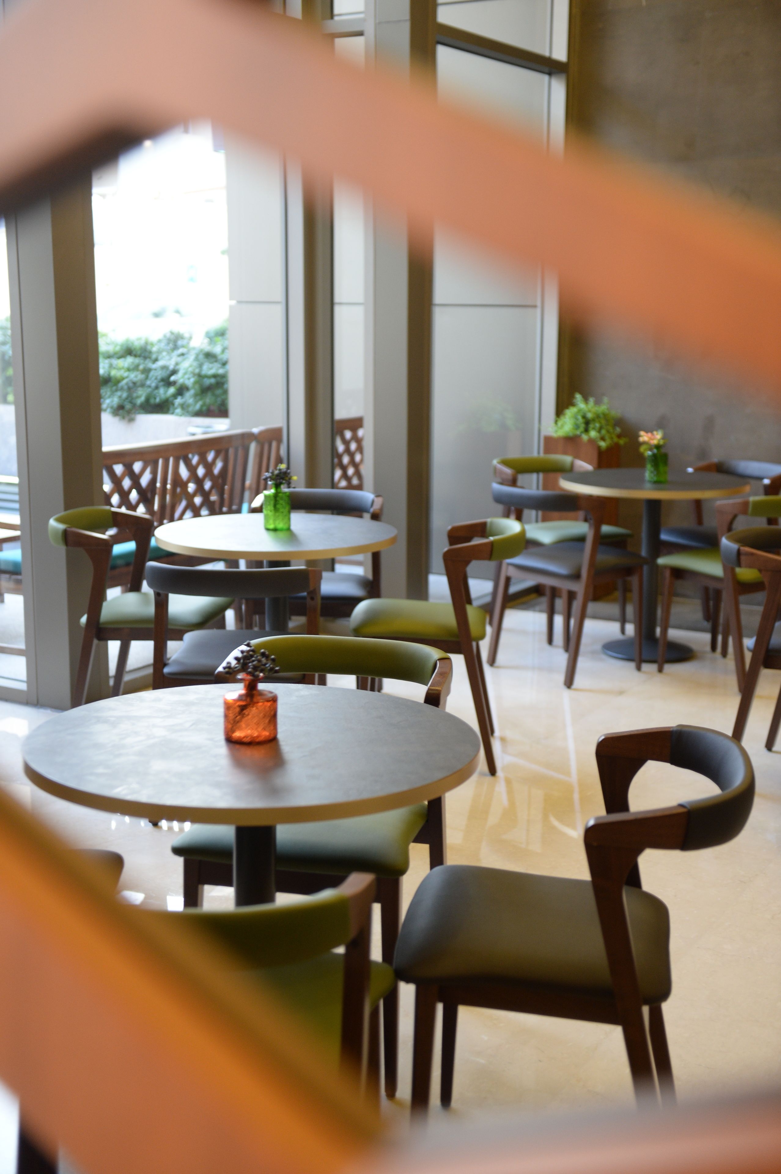 Una cafetería con mesas y sillas redondas, ventanas amplias y vistas a espacios verdes.