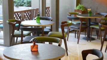 Una cafetería con mesas y sillas redondas, ventanas amplias y vistas a espacios verdes.