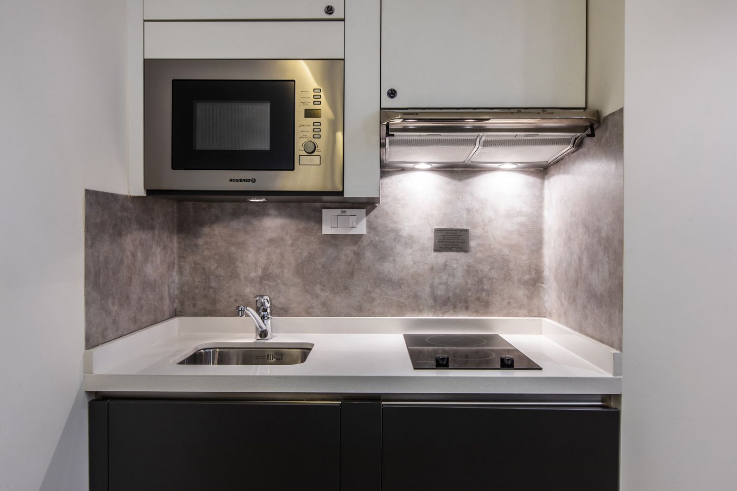Una cocina compacta con microondas integrado, pileta de acero inoxidable y cocina a gas.