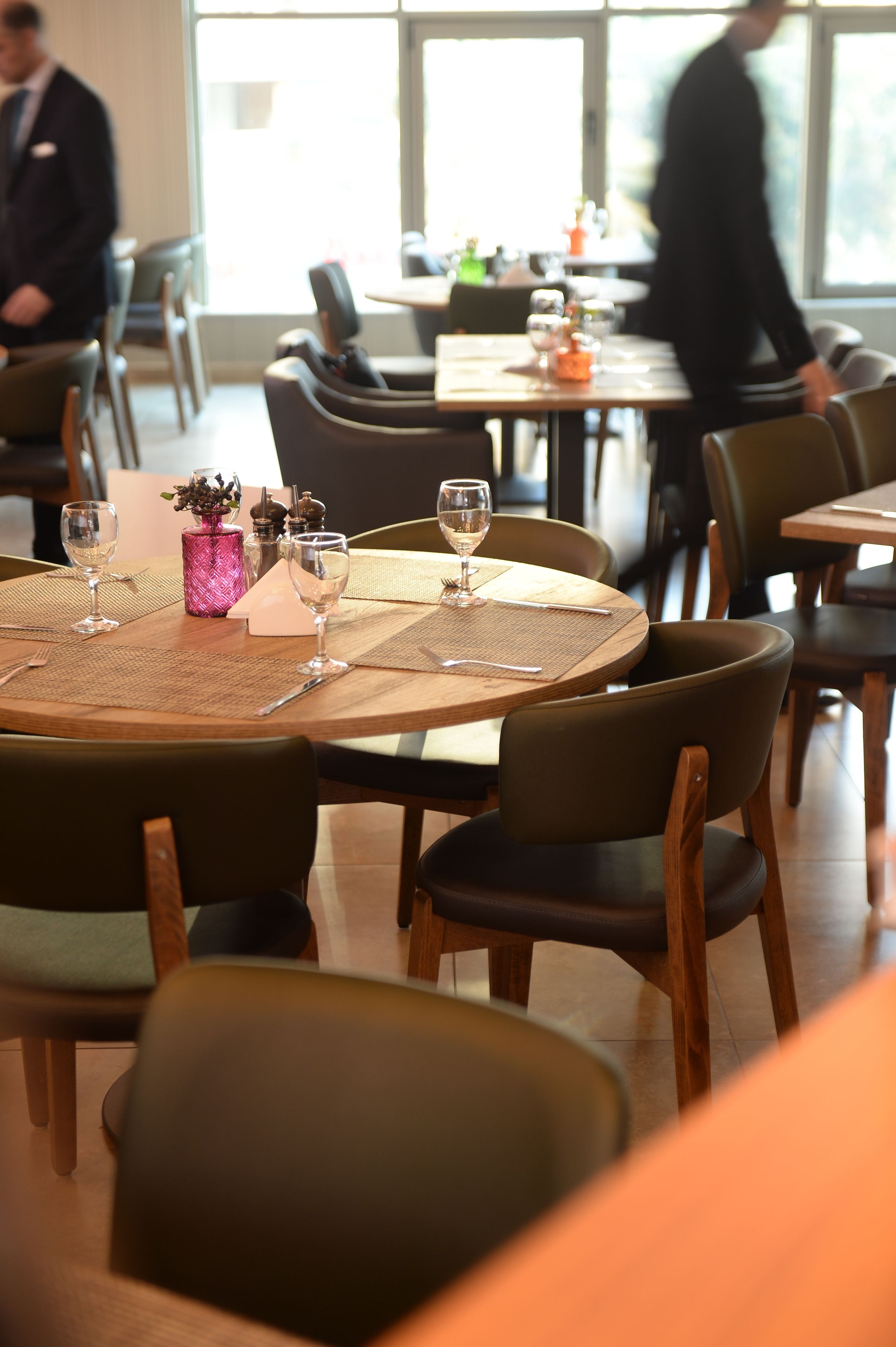 A restaurant with round tables set with wine glasses and a pink vase.
