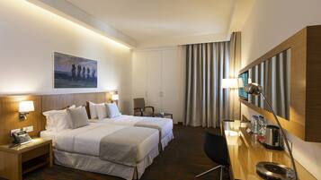 A hotel room with two beds, a desk, a chair, a telephone, a lamp, and a painting on the wall.