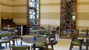 A dining area with multiple tables and chairs, a decorative wooden partition, and a staircase in the background.