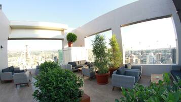 A rooftop terrace with modern furniture, large windows, and potted plants.