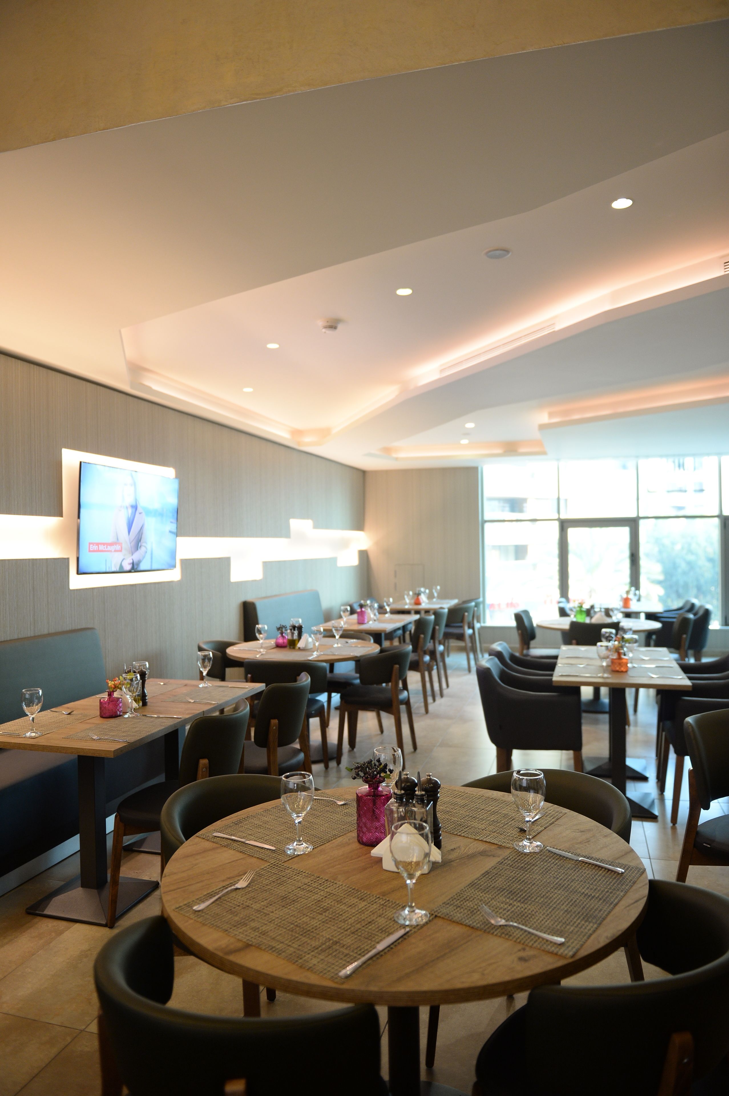 A modern dining area with round tables, chairs, and a flat-screen TV mounted on the wall.