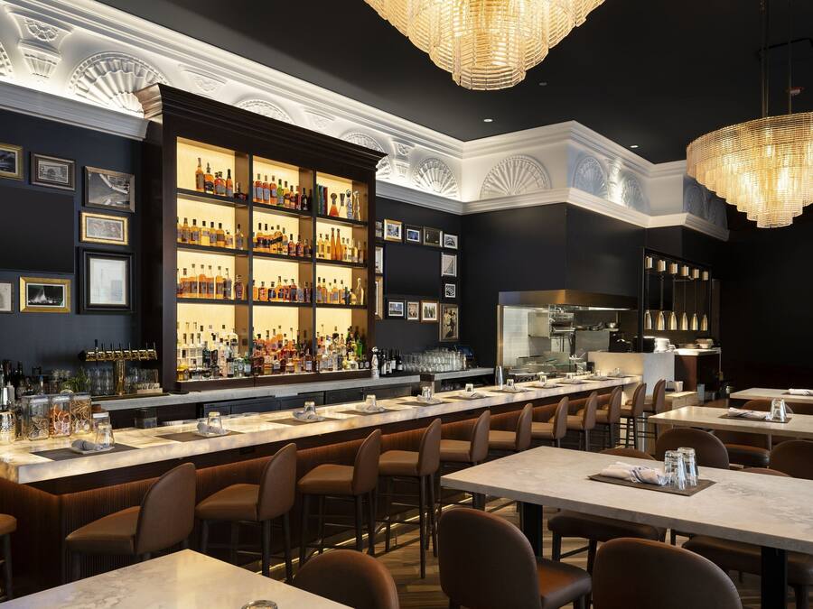 A bar area with a long counter, multiple seating options, and a well-stocked liquor display.