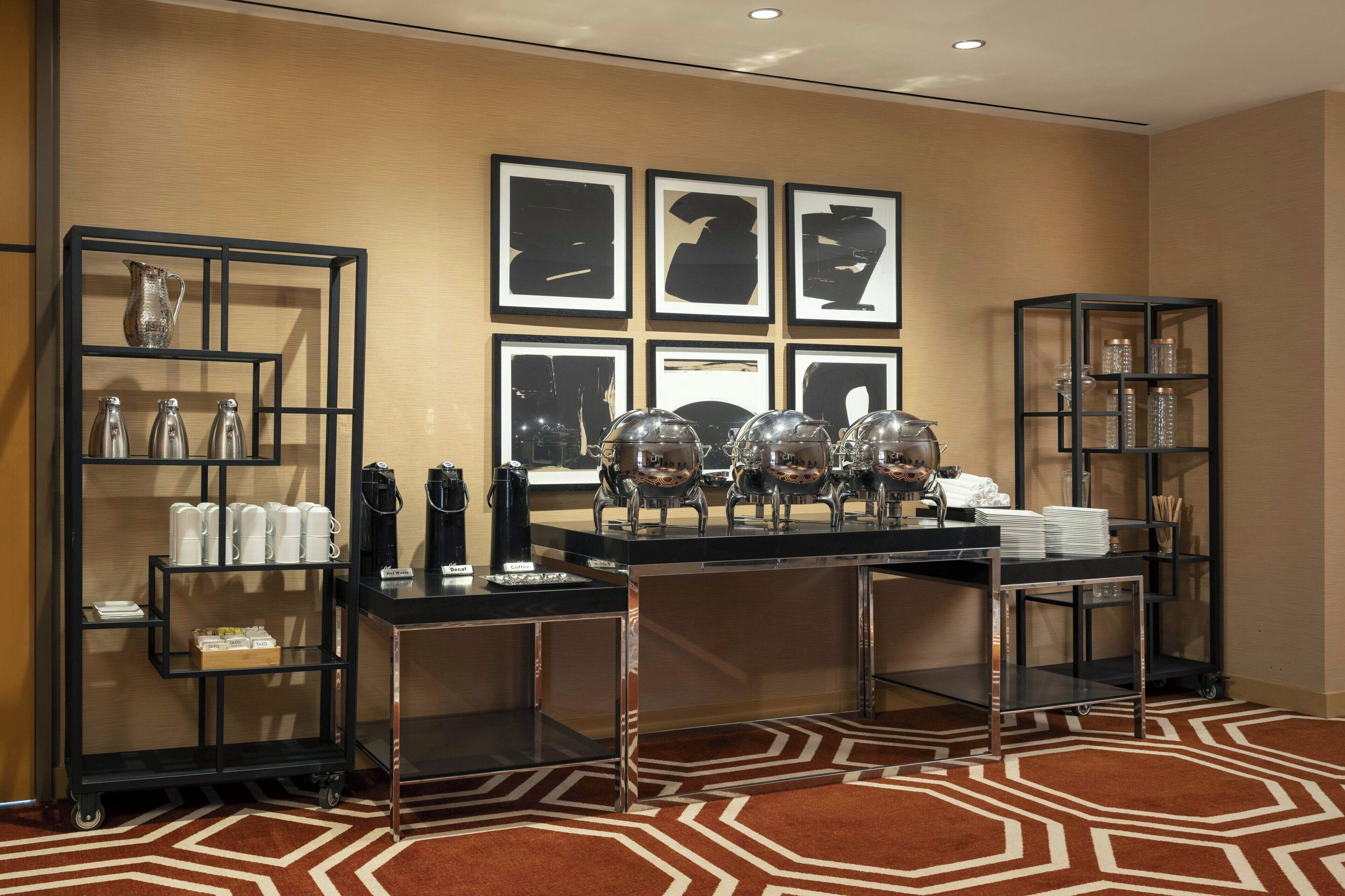 Une chambre d’hôtel avec une console en métal noir, des étagères en verre et un tapis à motifs.