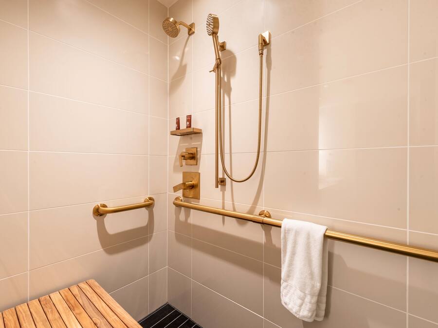 A bathroom with a shower, grab bars, a towel rack, and a wooden bench.