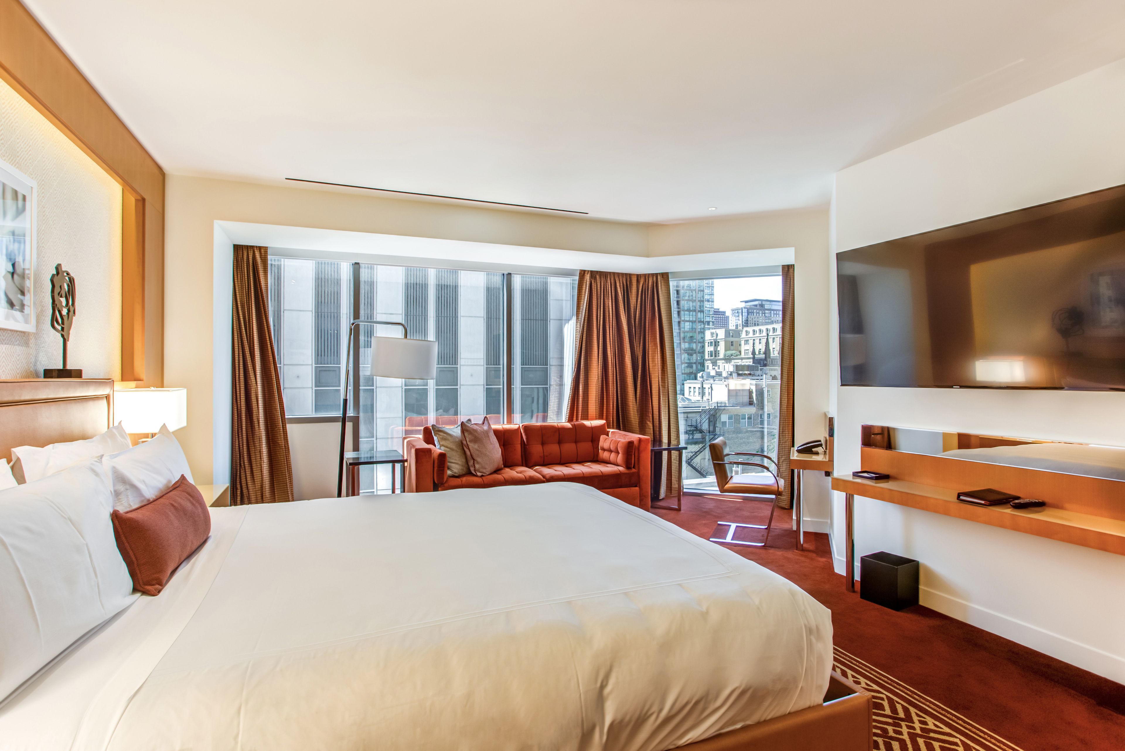 A hotel room with a large bed, a sofa, a TV, and a balcony with a city view.