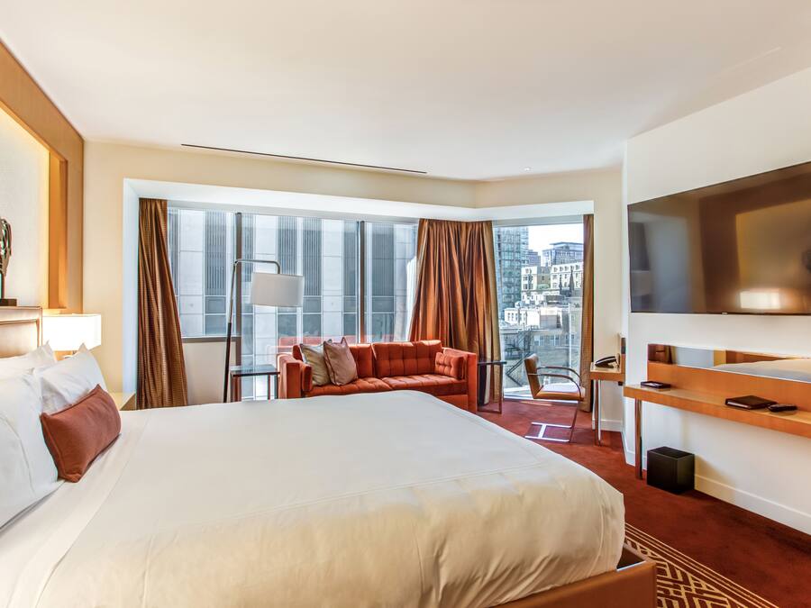 Ein Hotelzimmer mit einem großen Bett, einer Couch, einem Fernseher und einem Balkon mit Blick auf die Stadt.