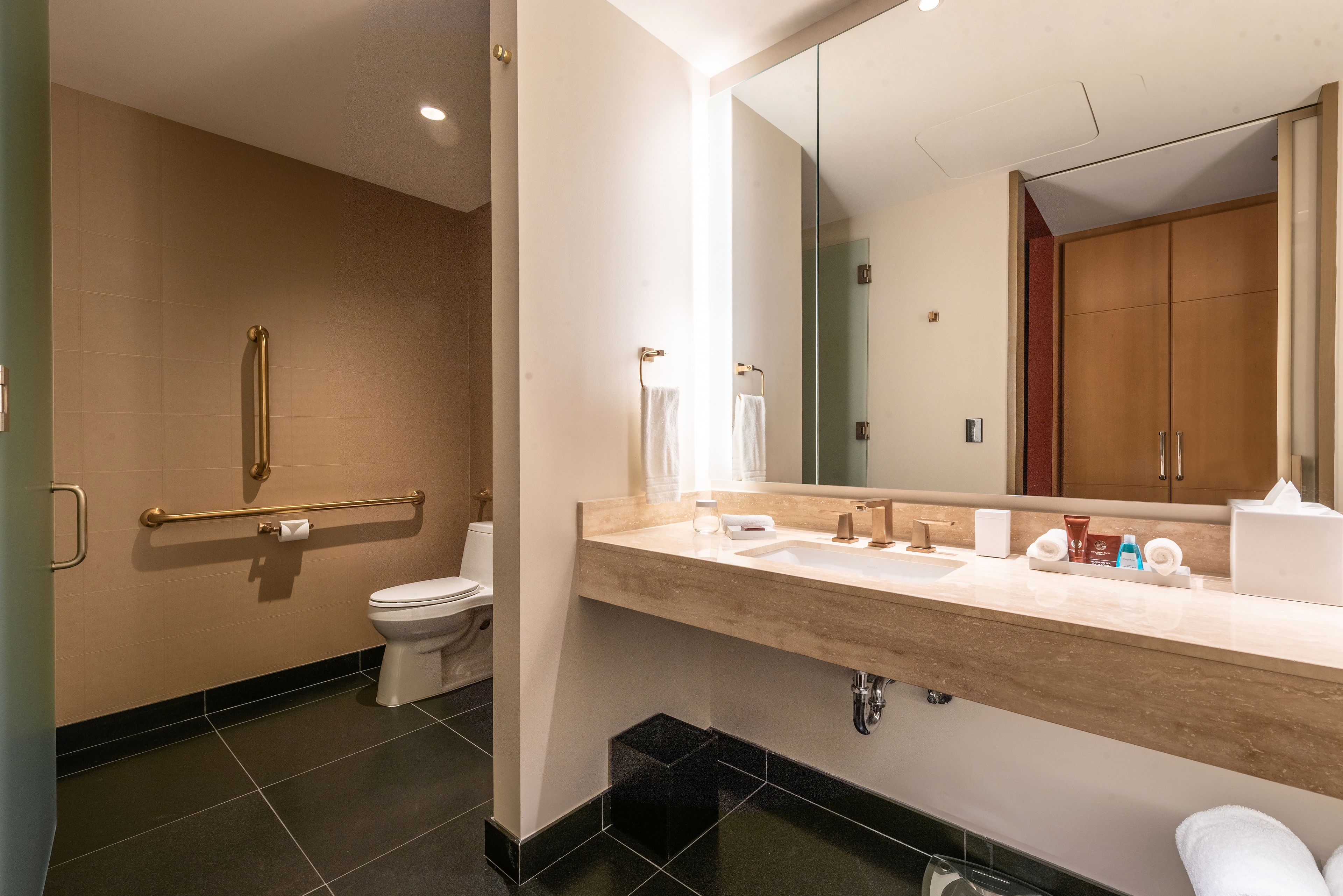 A modern bathroom with a beige tiled wall, a white toilet, a sink with a mirror, and a wooden cabinet.