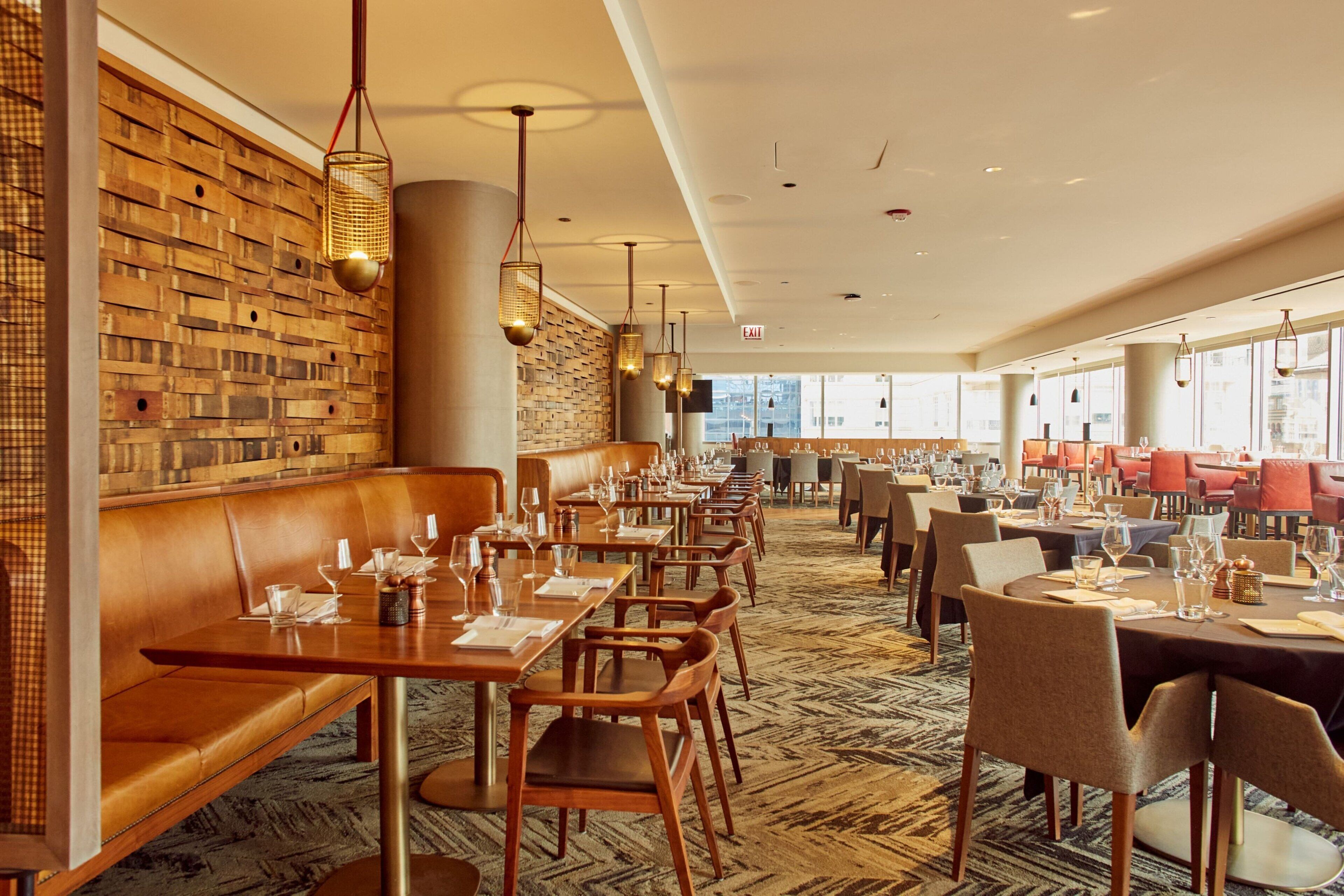 Un restaurant aux murs en bois, avec des banquettes en cuir et des tables dressées pour le service.