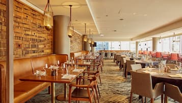 Un restaurant aux murs en bois, avec des banquettes en cuir et des tables dressées pour le service.