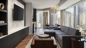 A modern living room with a large sectional sofa, a flat-screen TV mounted on the wall, a dining area with a table and chairs, and a view of the cityscape through large windows. - Residence Inn Chicago Downtown Magnificent Mile (Chicago)