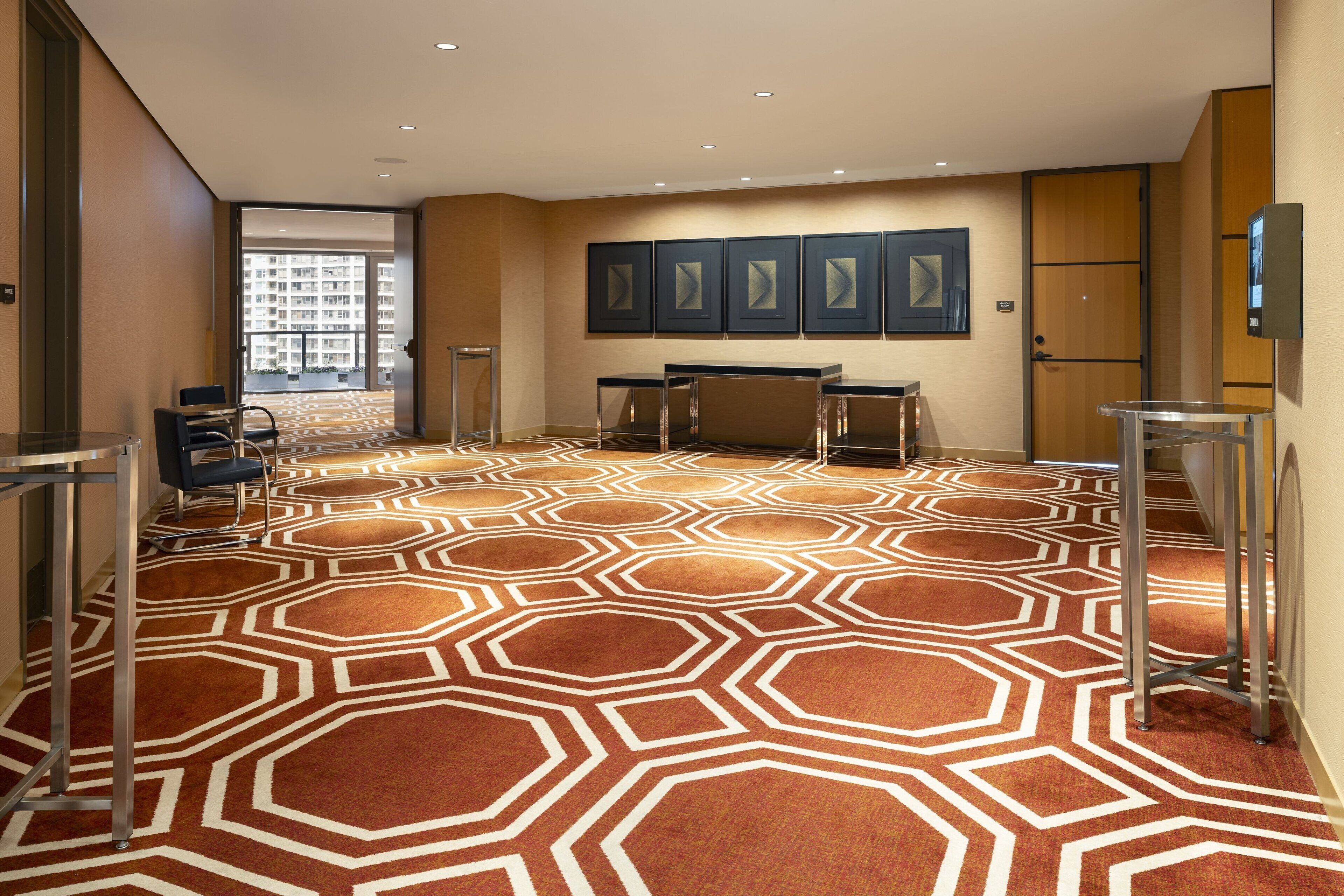 A hotel lobby with a geometric patterned carpet, a reception desk, and framed artwork on the wall.