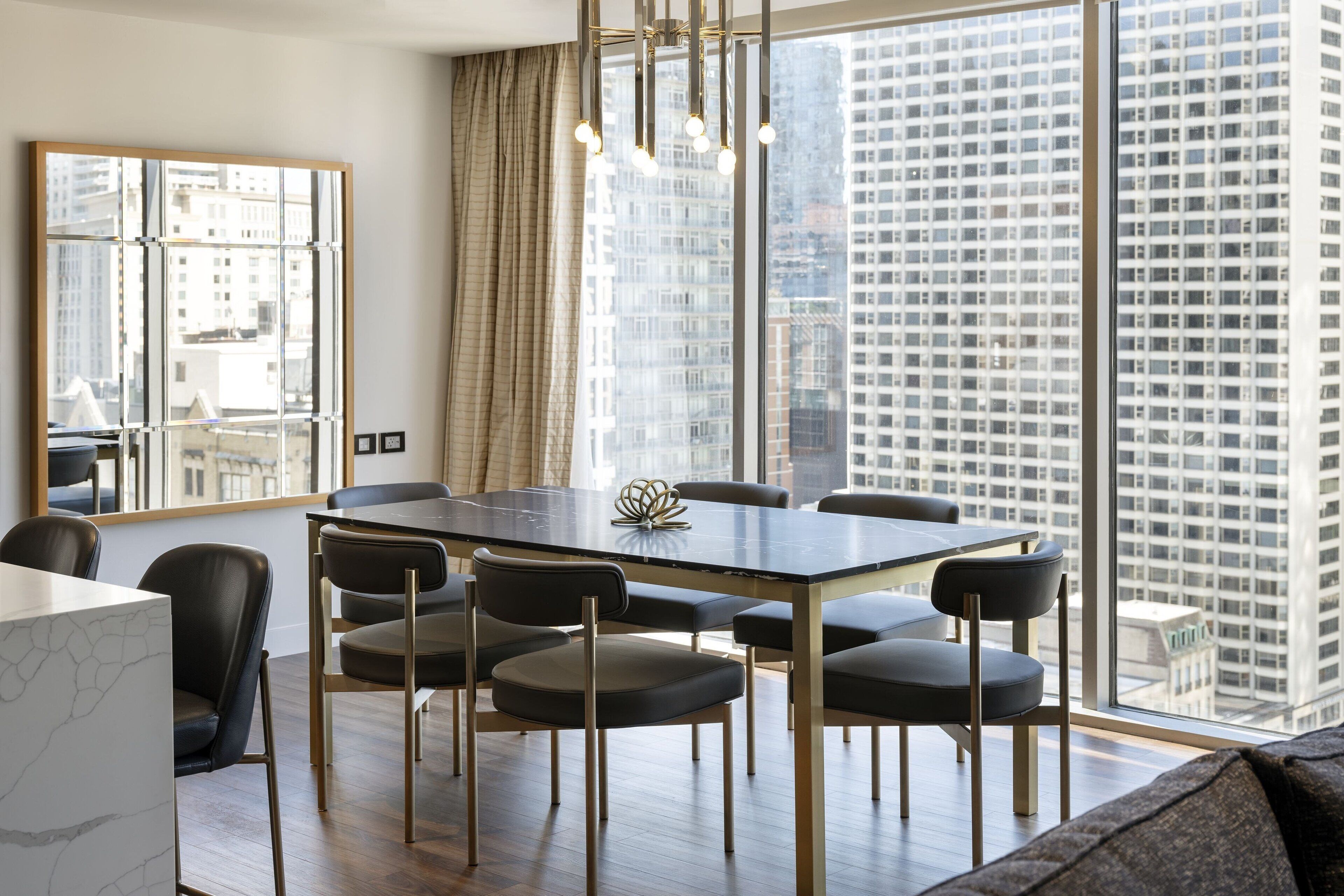 A modern dining area with a large table, chairs, and a view of a cityscape through large windows.