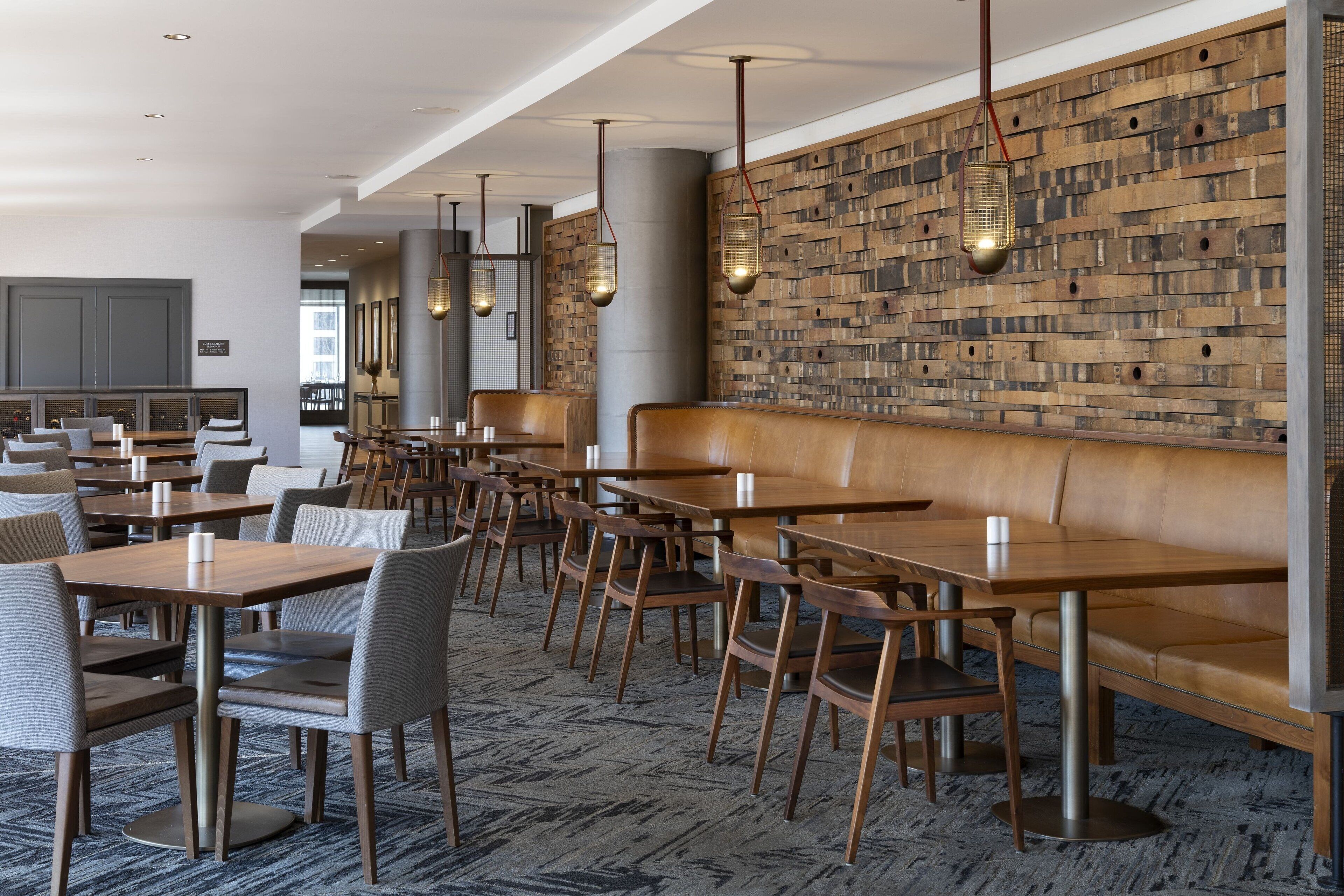 A modern dining area with wooden tables and chairs, a long bench, and hanging pendant lights.