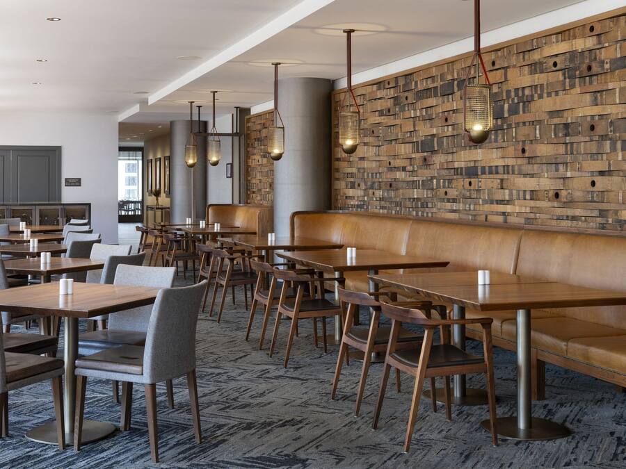 A modern dining area with wooden tables and chairs, a long bench, and hanging pendant lights.
