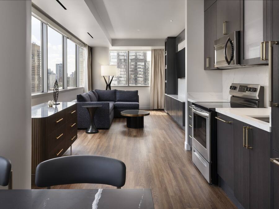 A modern kitchen with dark cabinetry, stainless steel appliances, and a large window providing a view of the cityscape.