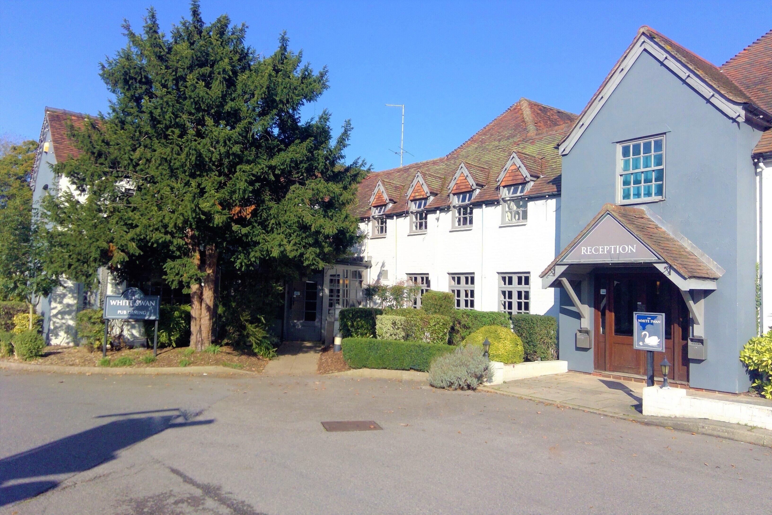 A building with a reception area, a sign for 'White Swan Pub', and a large tree in front.