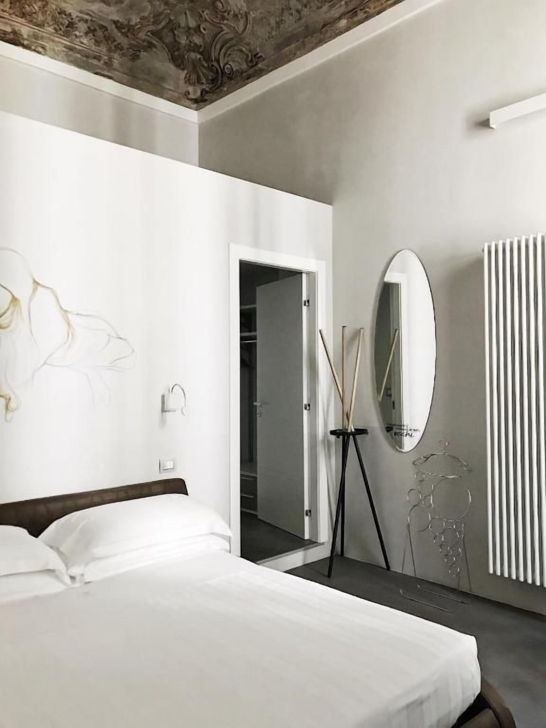A hotel room with a bed, a mirror, a radiator, and a door leading to a hallway.