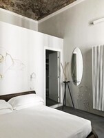 Quarto de hotel com cama, espelho, radiador e porta para um corredor.
