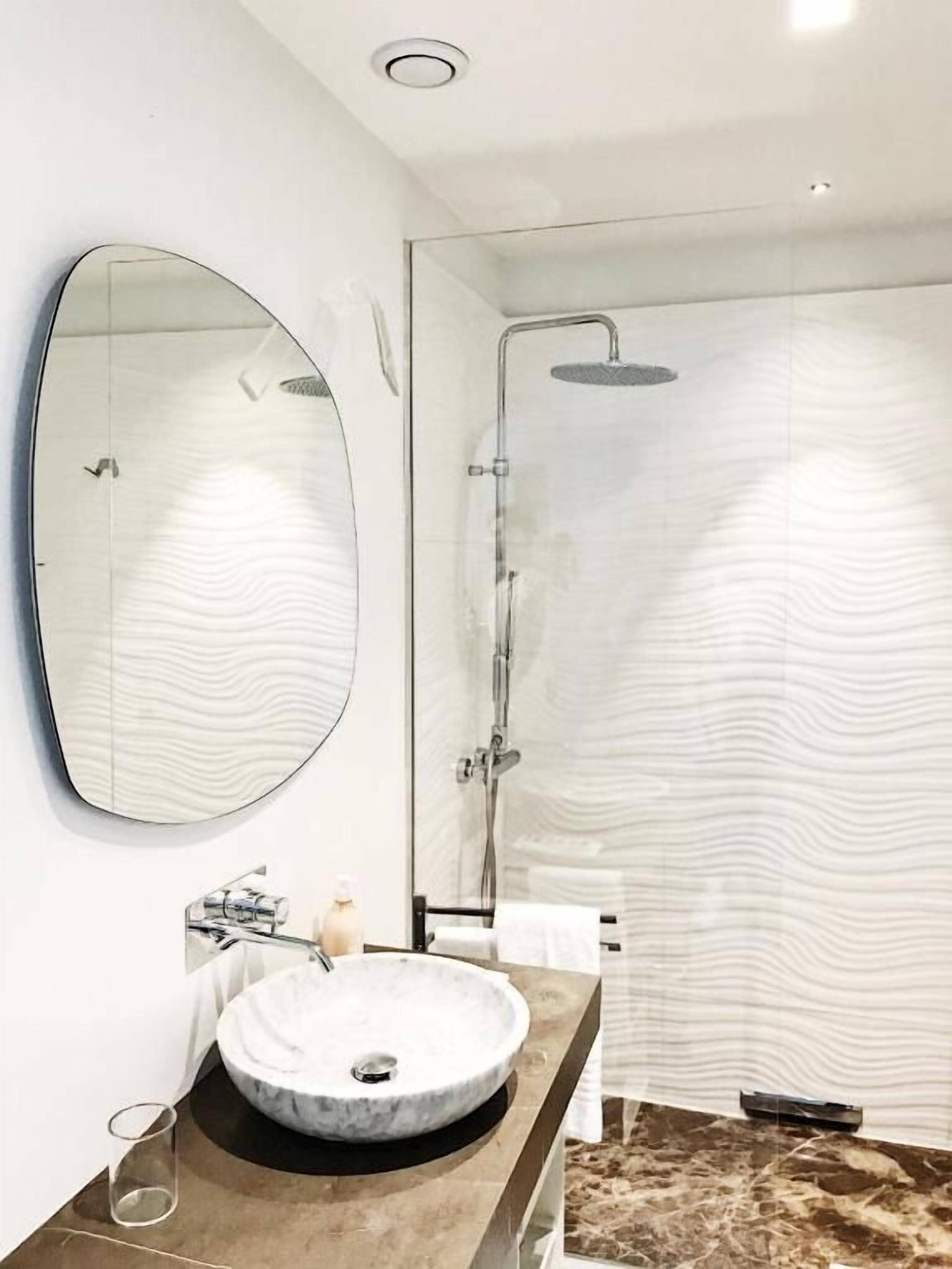 Une salle de bain moderne avec un lavabo rond, un grand miroir et une douche à parois de verre.