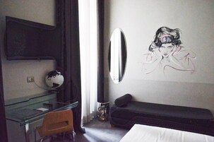 A hotel room with a glass desk, a black sofa, a wall-mounted mirror, and a globe on the desk.