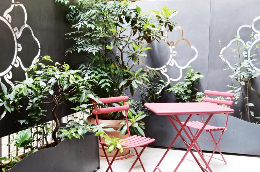 A red folding table and chair set on a balcony with potted plants and a decorative wall.
