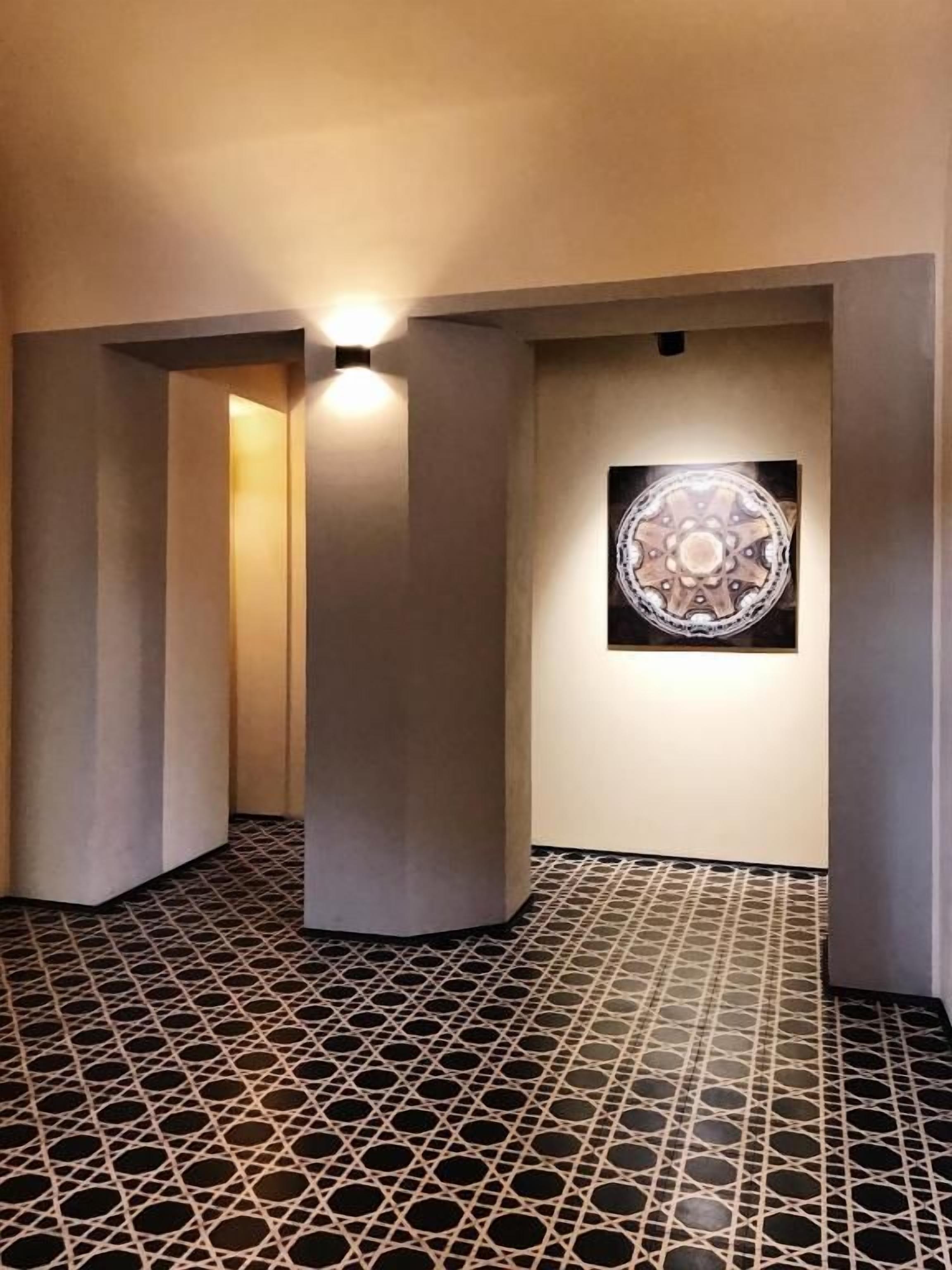 A hallway with a patterned floor, a wall-mounted light fixture, and a framed artwork.