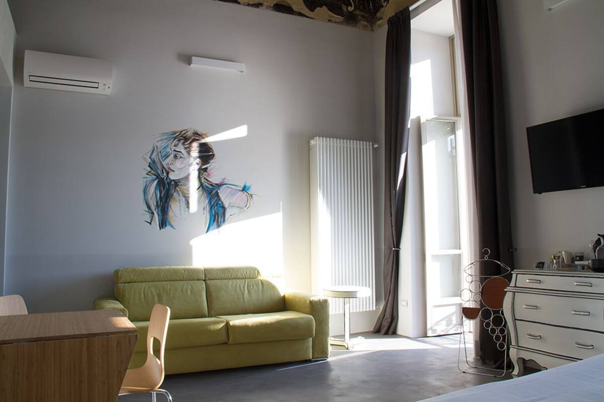 Une chambre d’hôtel moderne avec un canapé vert, une table en bois, un téléviseur et un radiateur.