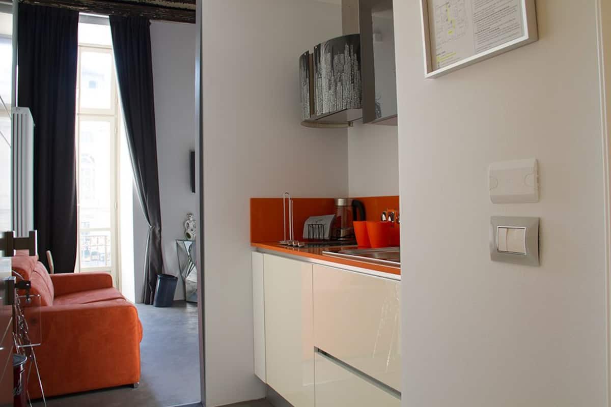Une cuisine moderne avec des meubles blancs, un plan de travail orange et une hotte noire.