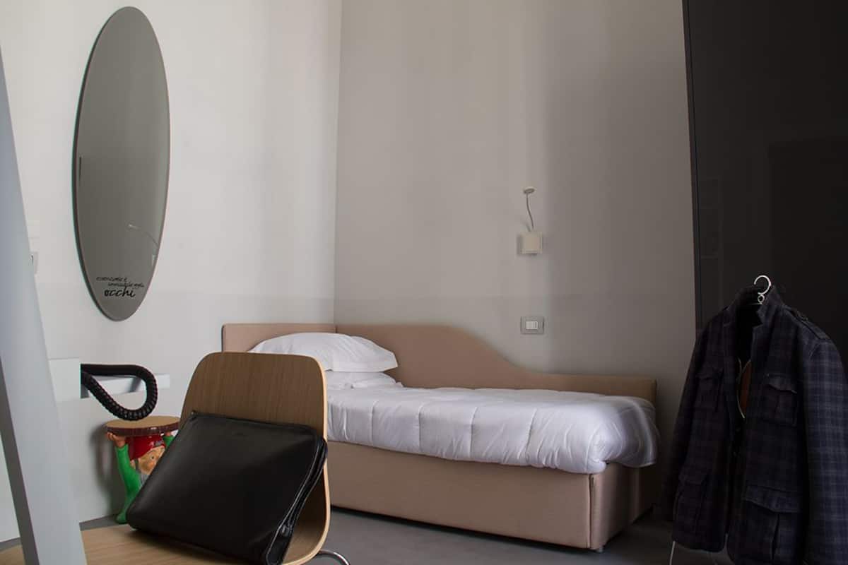 Une chambre à coucher comprenant un lit, une chaise, un porte-manteau et un miroir fixé au mur.