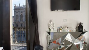 A modern hotel room with a large TV, a glass console table, and a view of a historic building. - Piazza Castello Suite (Turin)
