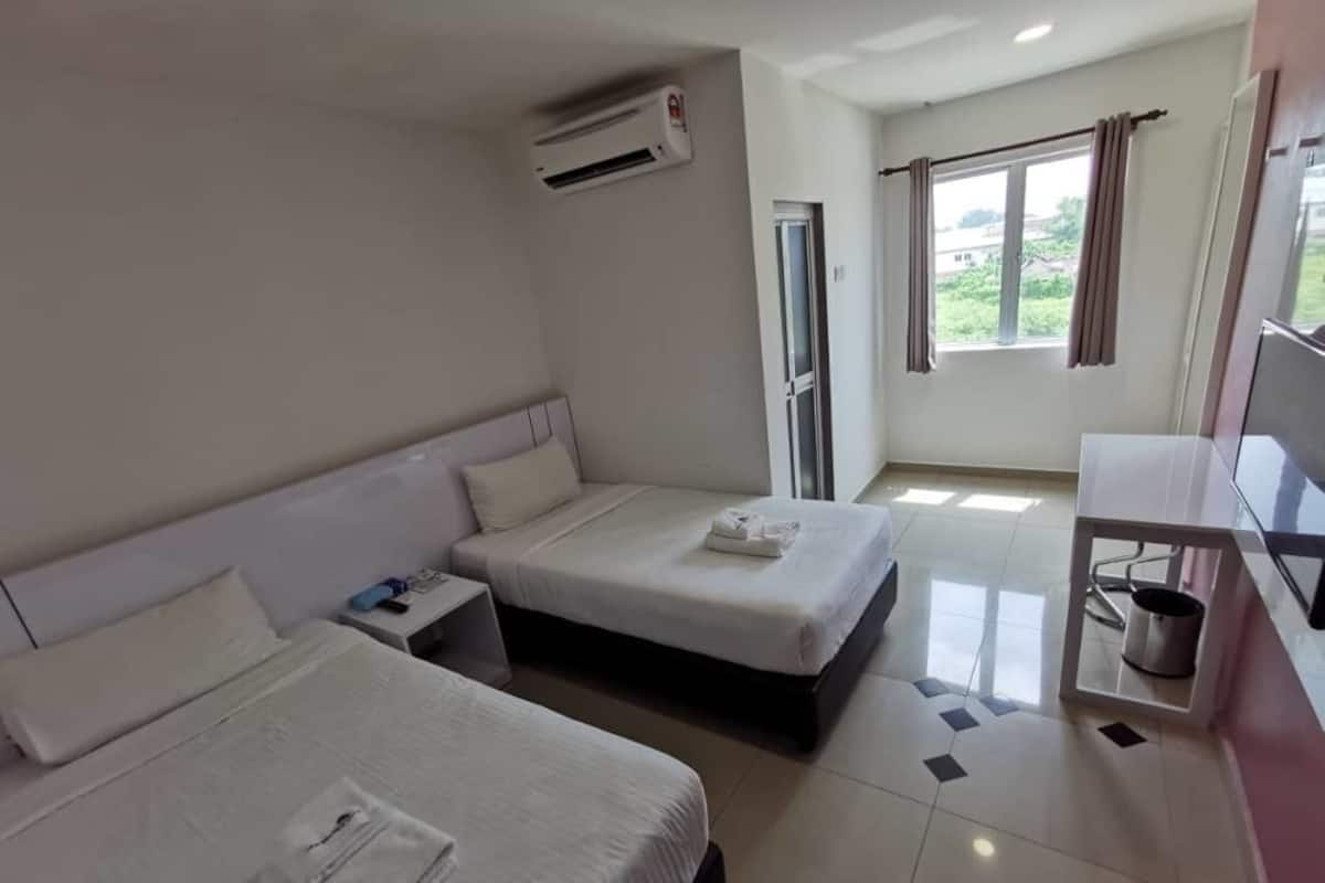 A hotel room with two beds, a TV, a small table, an air conditioning unit, and a window with curtains.