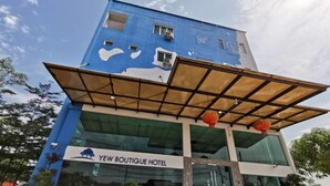 A modern hotel with a blue facade, a glass entrance, and a sign reading "Yew Boutique Hotel".