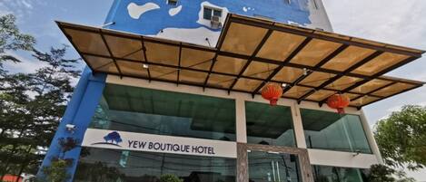 A modern hotel with a blue facade, a glass entrance, and a sign reading "Yew Boutique Hotel".