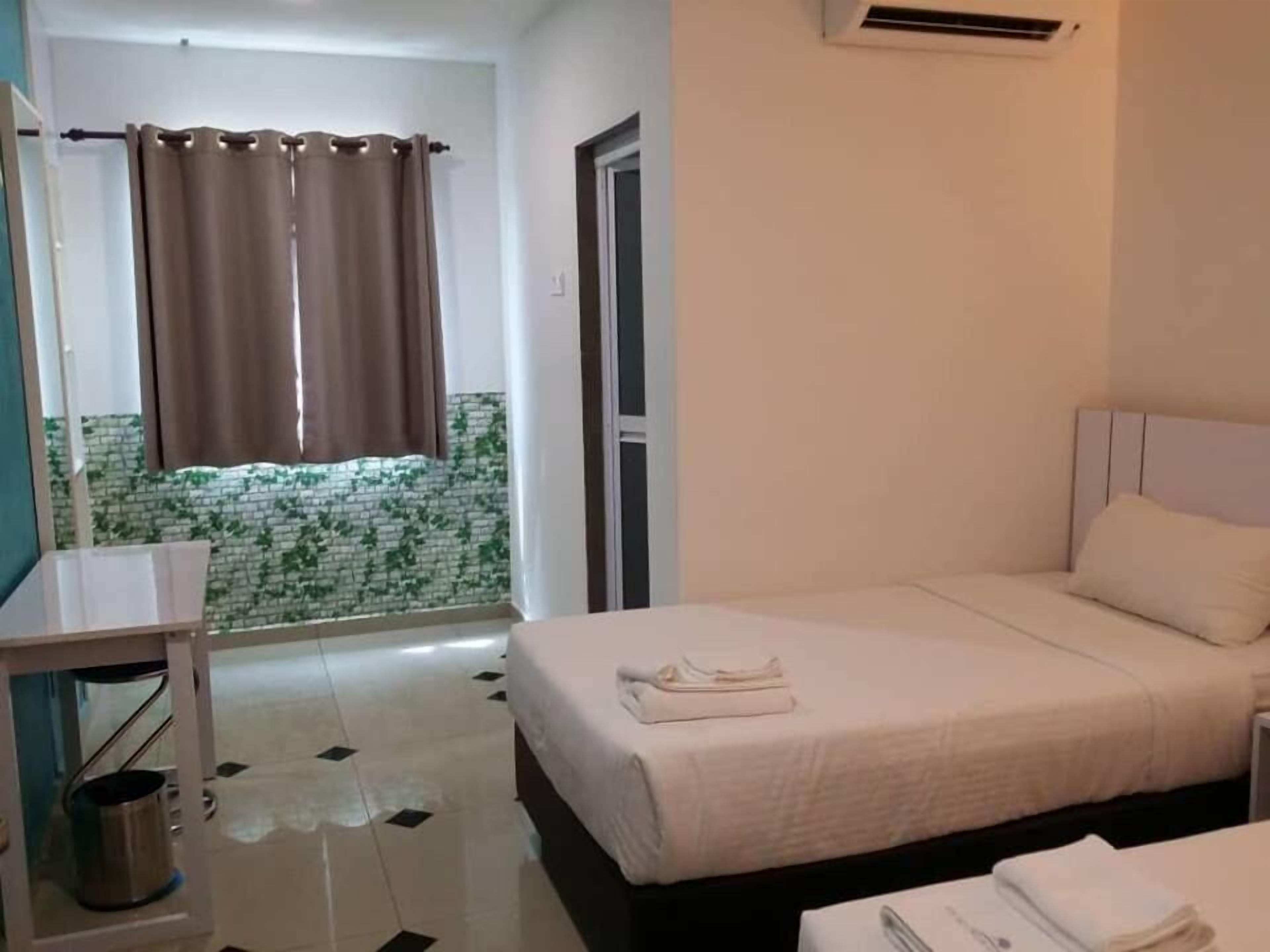 A hotel room with a bed, a bedside table, a mirror, a window with curtains, and a wall-mounted air conditioner.