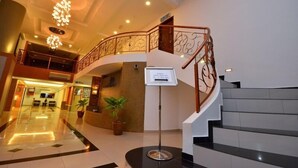 A hotel lobby with a grand staircase, a reception desk, and a chandelier.