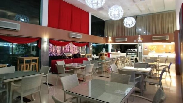 A spacious indoor dining area with multiple tables and chairs, a red accent wall, and decorative spherical light fixtures on the ceiling.