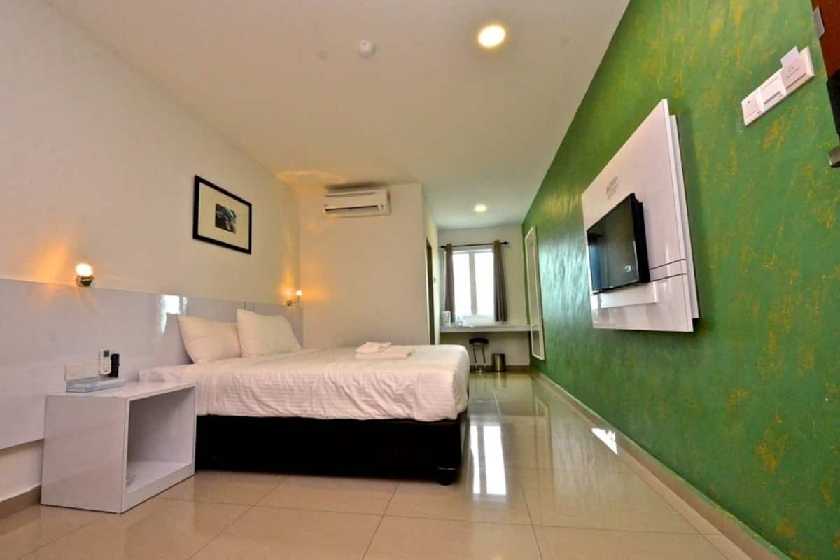 A hotel room with a bed, bedside table, air conditioning unit, and a television mounted on the wall.
