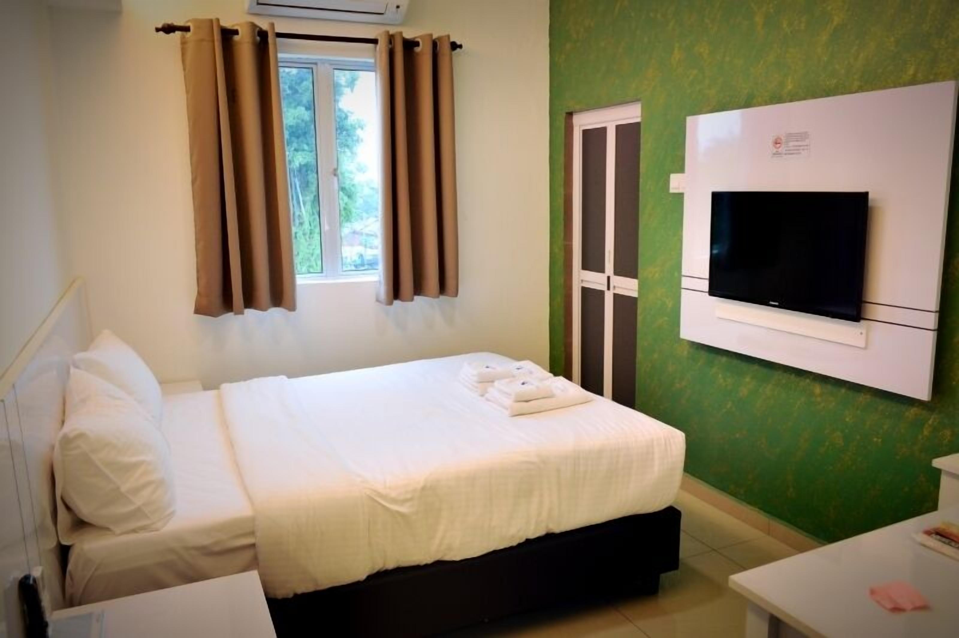 A hotel room with a bed, a TV mounted on the wall, and a window with curtains.