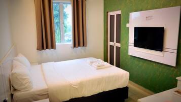 A hotel room with a bed, a TV mounted on the wall, and a window with curtains.