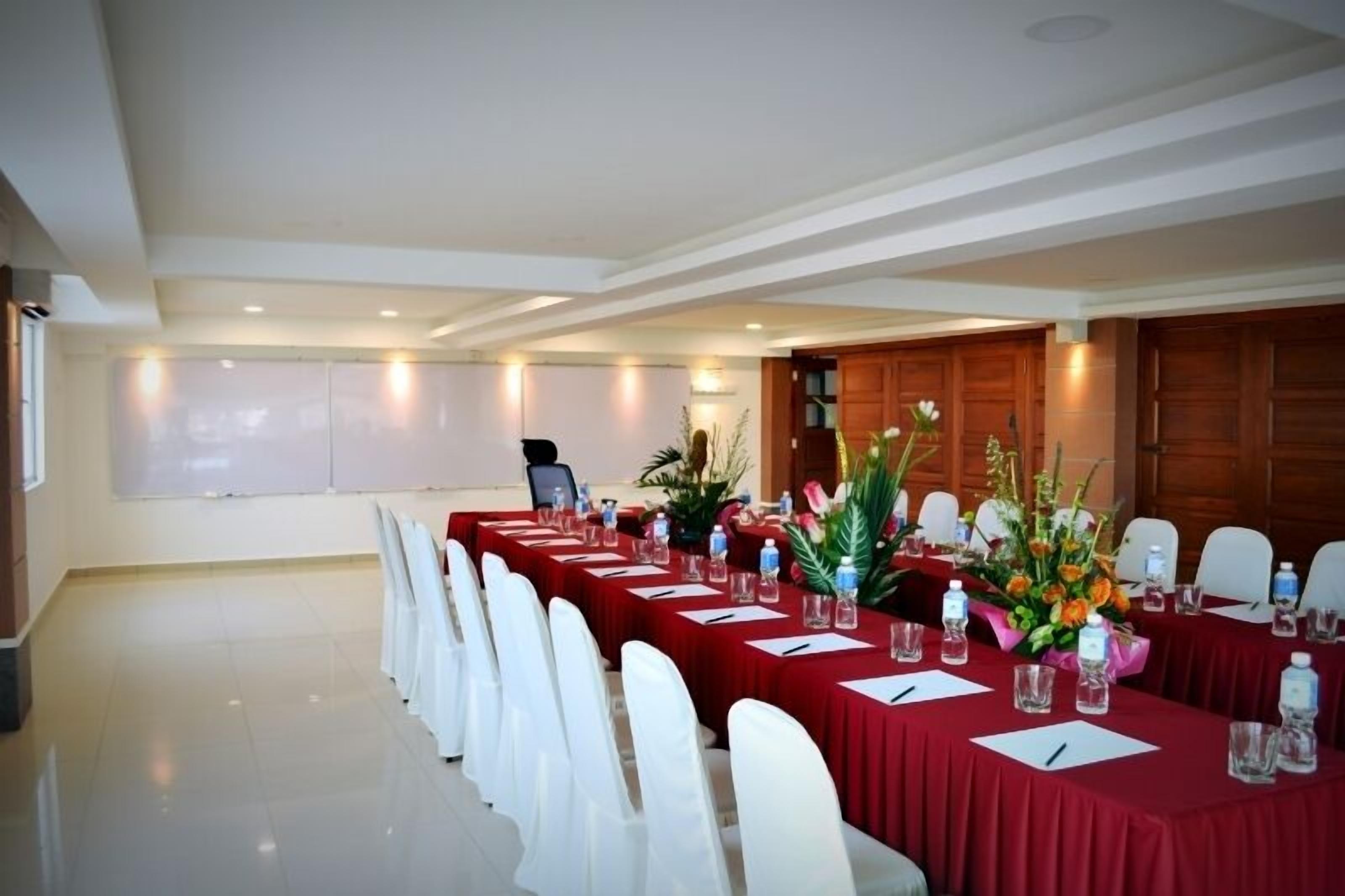 A conference room with long tables, white chairs, and floral centerpieces.